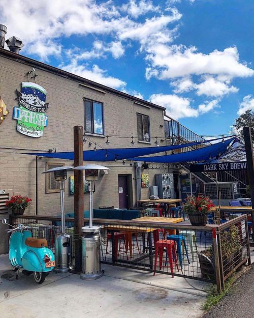 A vibrant outdoor seating area of a restaurant with colorful chairs, a blue awning, and a vintage scooter parked nearby.