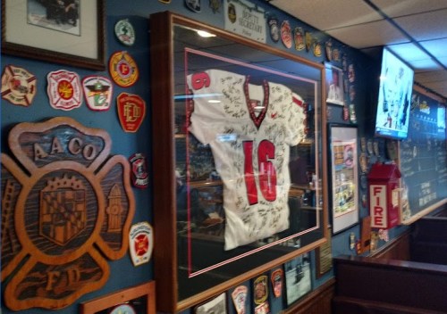 Framed signed football jersey displayed on a wall adorned with various badges and memorabilia in a restaurant.