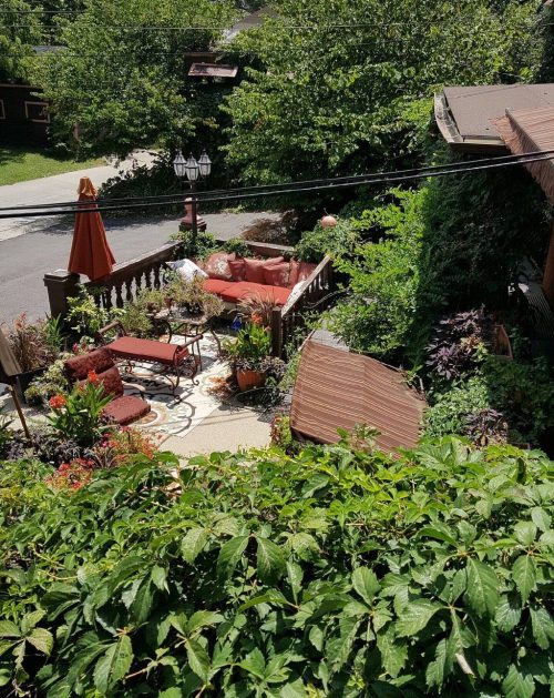 A lush garden with patio furniture, surrounded by greenery and trees, viewed from above.