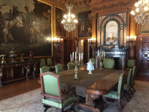 Elegant dining room with a large table, ornate chairs, chandeliers, and historical paintings on the walls.