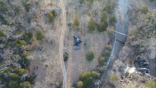 Aerial view of a winding path through a wooded area near a river, with a large rock formation visible on the ground.