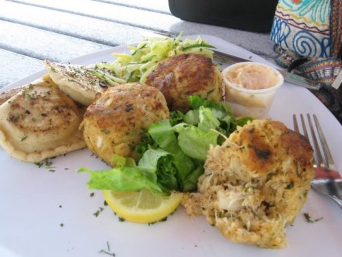 A plate of crab cakes, salad, and lemon slices, served with a side of dipping sauce on a table.