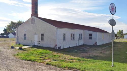 A single-story building with a red roof, chimney, and grassy area, near a road sign in a rural setting.