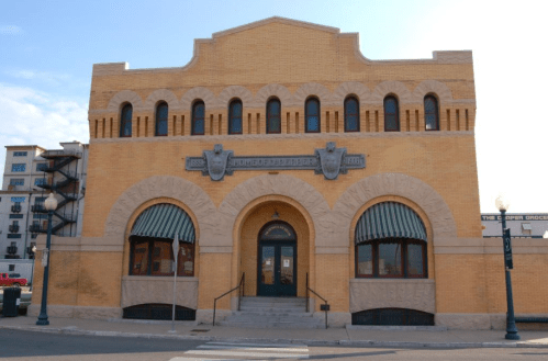 Historic yellow brick building with arched windows and decorative stonework, featuring a central entrance and awnings.