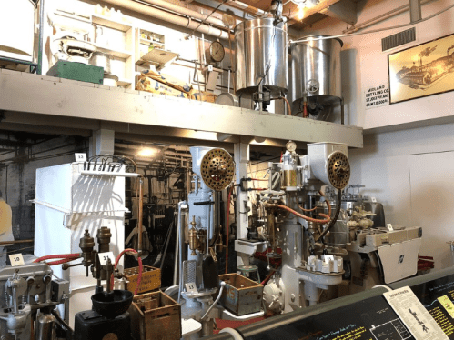 A collection of vintage machinery and equipment displayed in a museum setting, featuring various tanks and gauges.