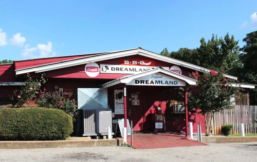 Exterior of Dreamland BBQ restaurant, featuring a red building with signage and a landscaped entrance.