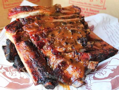 A stack of glazed, barbecued ribs on parchment paper, showcasing a rich, smoky sauce.
