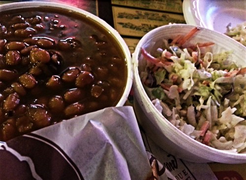 A bowl of baked beans next to a small container of coleslaw on a table.
