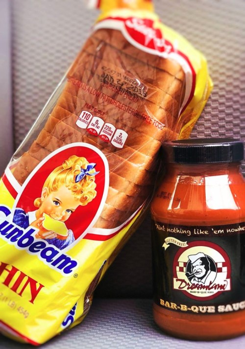 A loaf of Sunbeam bread next to a jar of Dreamland Bar-B-Que sauce on a textured surface.