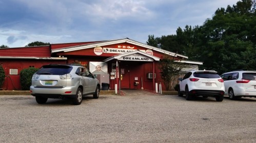 Exterior of Dreamland BBQ restaurant with parked cars in front and a cloudy sky above.