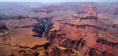 Aerial view of the Grand Canyon, showcasing its layered rock formations and winding river below.
