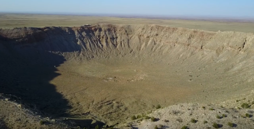 Aerial view of a large, dry crater surrounded by flat terrain under a clear blue sky.