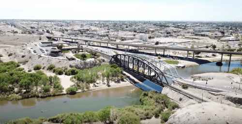 Aerial view of a cityscape featuring a bridge over a river, surrounded by greenery and urban development.
