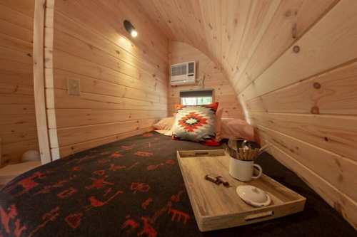Cozy wooden interior of a tiny home with a bed, decorative pillow, and a tray with pens and a small dish.