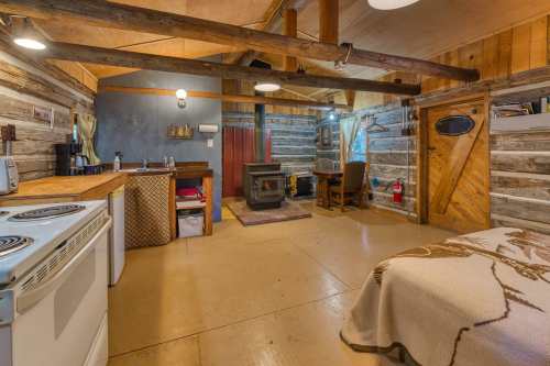 Cozy cabin interior with wooden beams, a kitchenette, a small dining area, and a wood stove. Warm and rustic atmosphere.
