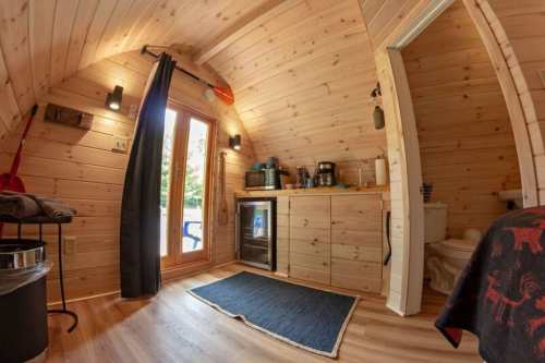 Cozy interior of a wooden tiny home featuring a kitchenette, bathroom, and large windows for natural light.