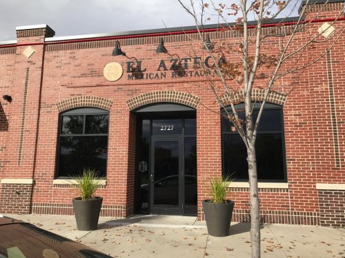 Exterior of El Azteca Mexican Restaurant, featuring a brick facade, large windows, and potted plants.