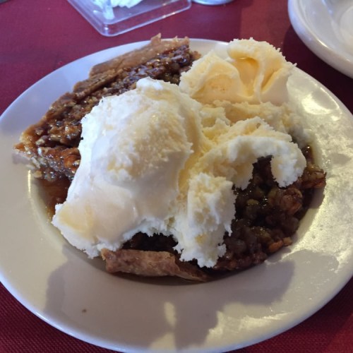 A slice of pie topped with a scoop of vanilla ice cream on a white plate.