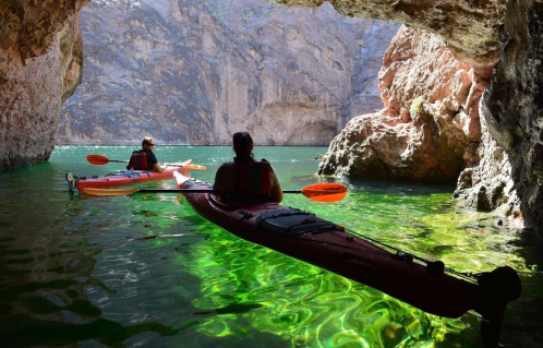 Two kayakers explore a serene cave with vibrant green water and rocky walls in a tranquil setting.