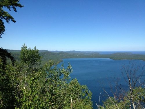 A scenic view of a calm blue lake surrounded by lush green hills under a clear blue sky.