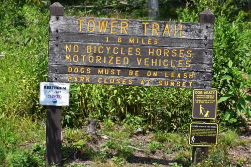 Sign for Tower Trail, indicating distance, rules for pets, and park hours, with additional signs for restrooms and dog waste.