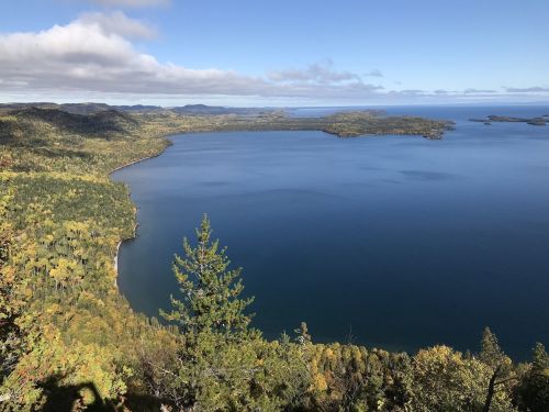 A scenic view of a calm lake surrounded by colorful autumn foliage and distant hills under a clear blue sky.