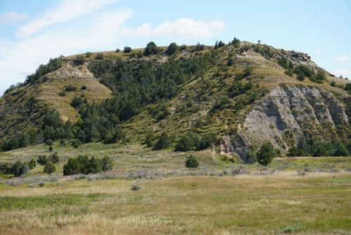A scenic view of rolling hills covered in greenery under a blue sky with scattered clouds.