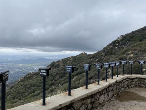Viewpoint with signs indicating distances to various locations, overlooking a mountainous landscape under cloudy skies.