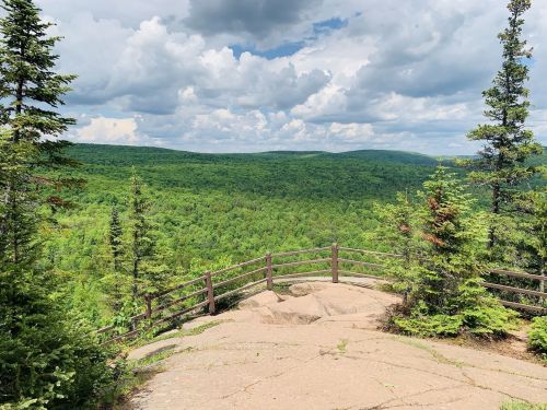 A scenic view from a rocky overlook, surrounded by lush green trees and a cloudy sky.