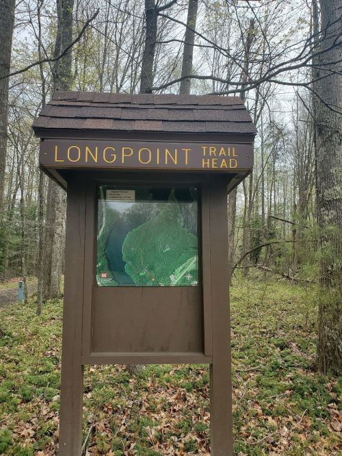Sign for Longpoint Trail Head with a map, surrounded by trees and greenery in a forested area.
