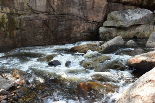 A rushing river flows over rocks, surrounded by rugged stone cliffs in a natural setting.