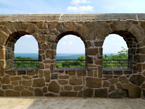 Stone archway with three openings, overlooking a scenic view of green hills and a blue sky.