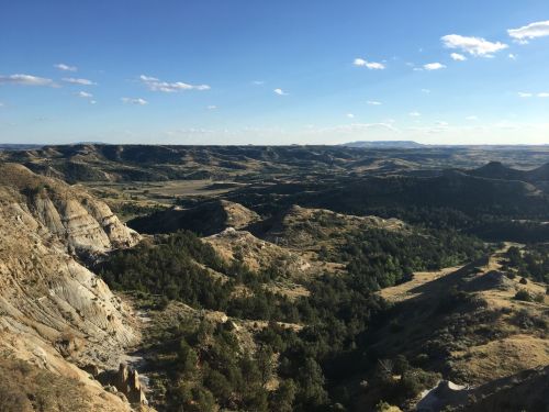 A panoramic view of rolling hills and valleys under a clear blue sky, with patches of greenery and rocky terrain.