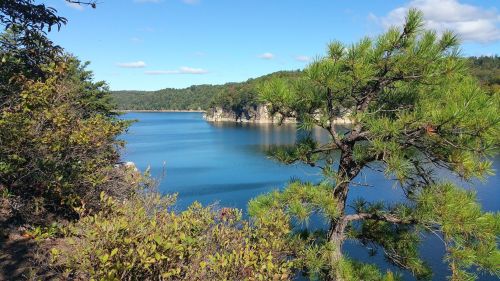 A serene lake surrounded by lush greenery and rocky cliffs under a clear blue sky.