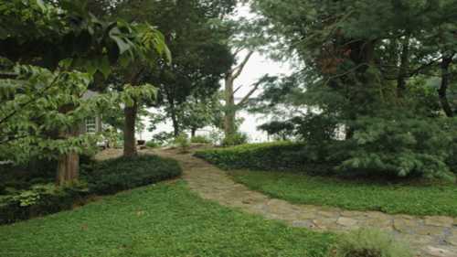 A serene garden path winding through lush greenery, leading to a tranquil water view in the background.