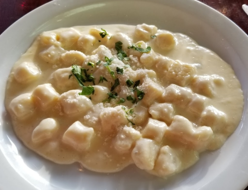 A plate of gnocchi in a creamy sauce, garnished with herbs and grated cheese.