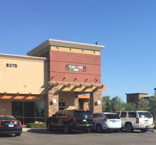 A commercial building with a sign reading "FABIO-FREE," surrounded by parked cars under a clear blue sky.