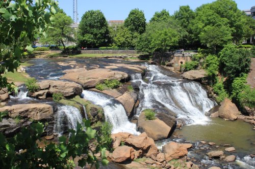 A scenic view of a waterfall cascading over rocky formations, surrounded by lush green trees and a clear blue sky.