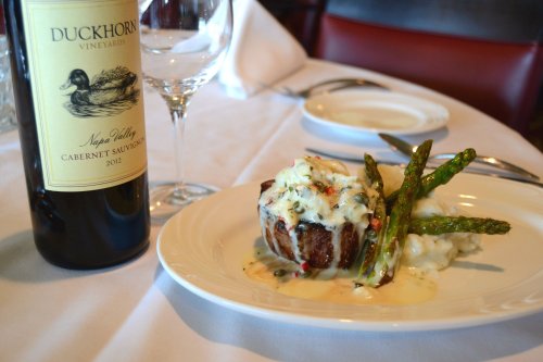 A plate with a gourmet steak topped with sauce, asparagus, and mashed potatoes, alongside a bottle of Duckhorn Cabernet Sauvignon.