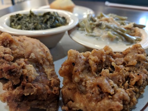 A plate featuring crispy fried chicken, collard greens, green beans, and a biscuit.