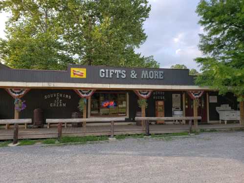 A rustic gift shop with a sign reading "Gifts & More," featuring ice cream and souvenirs, surrounded by greenery.