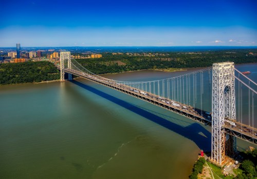 Aerial view of the George Washington Bridge spanning a river, with green hills and city buildings in the background.