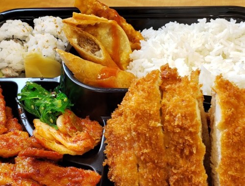 A bento box featuring rice, sushi, crispy chicken, and fried dumplings with a side of green salad.