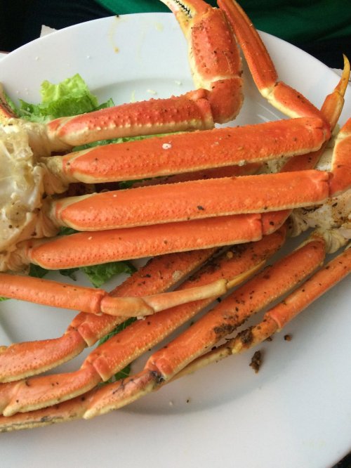 A close-up of a cooked crab with orange legs on a white plate, garnished with lettuce.