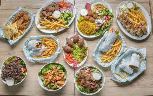 A variety of Mediterranean dishes including wraps, salads, fries, and appetizers arranged on a wooden table.
