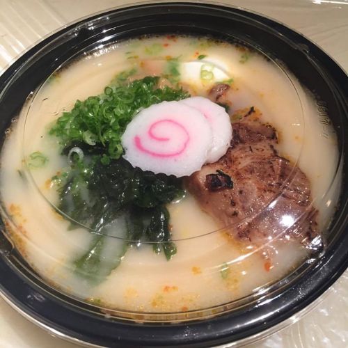 A bowl of ramen with creamy broth, sliced meat, green onions, seaweed, and a pink swirl fish cake on top.
