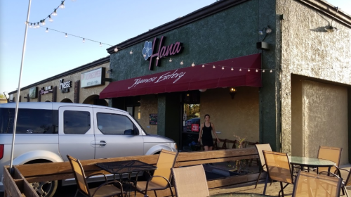 Exterior of Hana Japanese Eatery with a red awning, a parked white SUV, and outdoor seating under string lights.