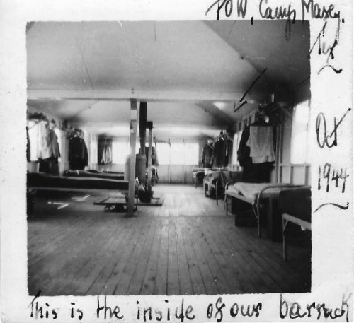 Interior of a barrack at POW Camp, with wooden floors, beds, and clothing hanging on hooks. Dated October 1944.
