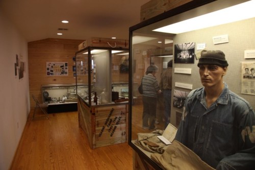 A museum exhibit featuring a mannequin in a prison uniform, display cases with artifacts, and informational panels.