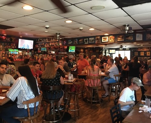 A busy bar filled with patrons enjoying drinks and food, with TVs showing sports and walls decorated with memorabilia.